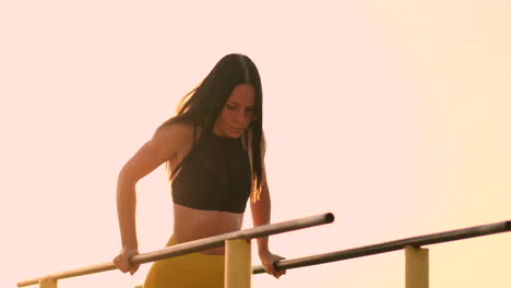 Slow-motion:-a-Beautiful-woman-athlete-doing-push-UPS-on-bars-in-a-black-tank-top-in-great-shape-and-yellow-pants-with-dark-hair.